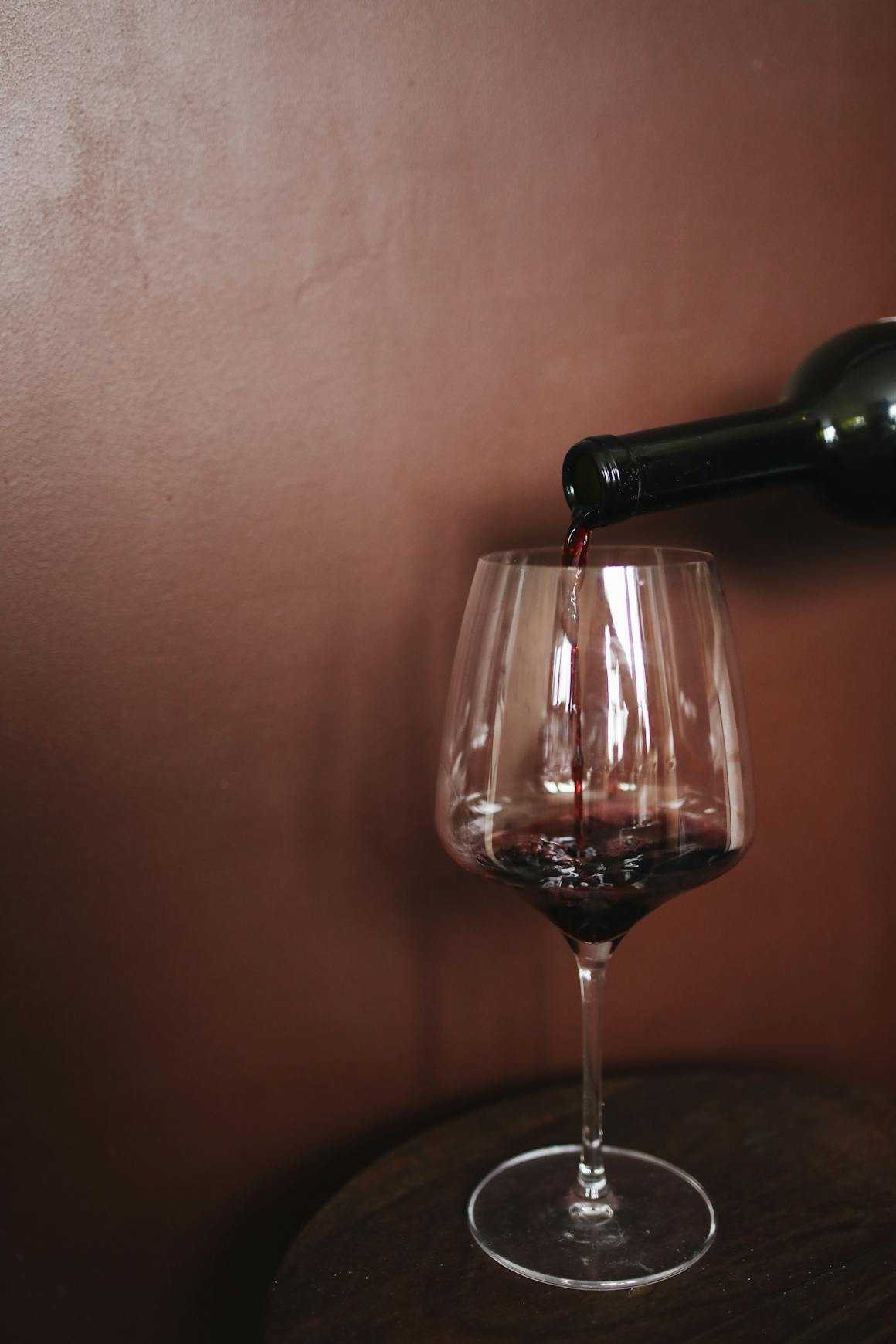 Close-up of red wine being poured into a glass against a warm, brown background, creating a luxurious atmosphere.