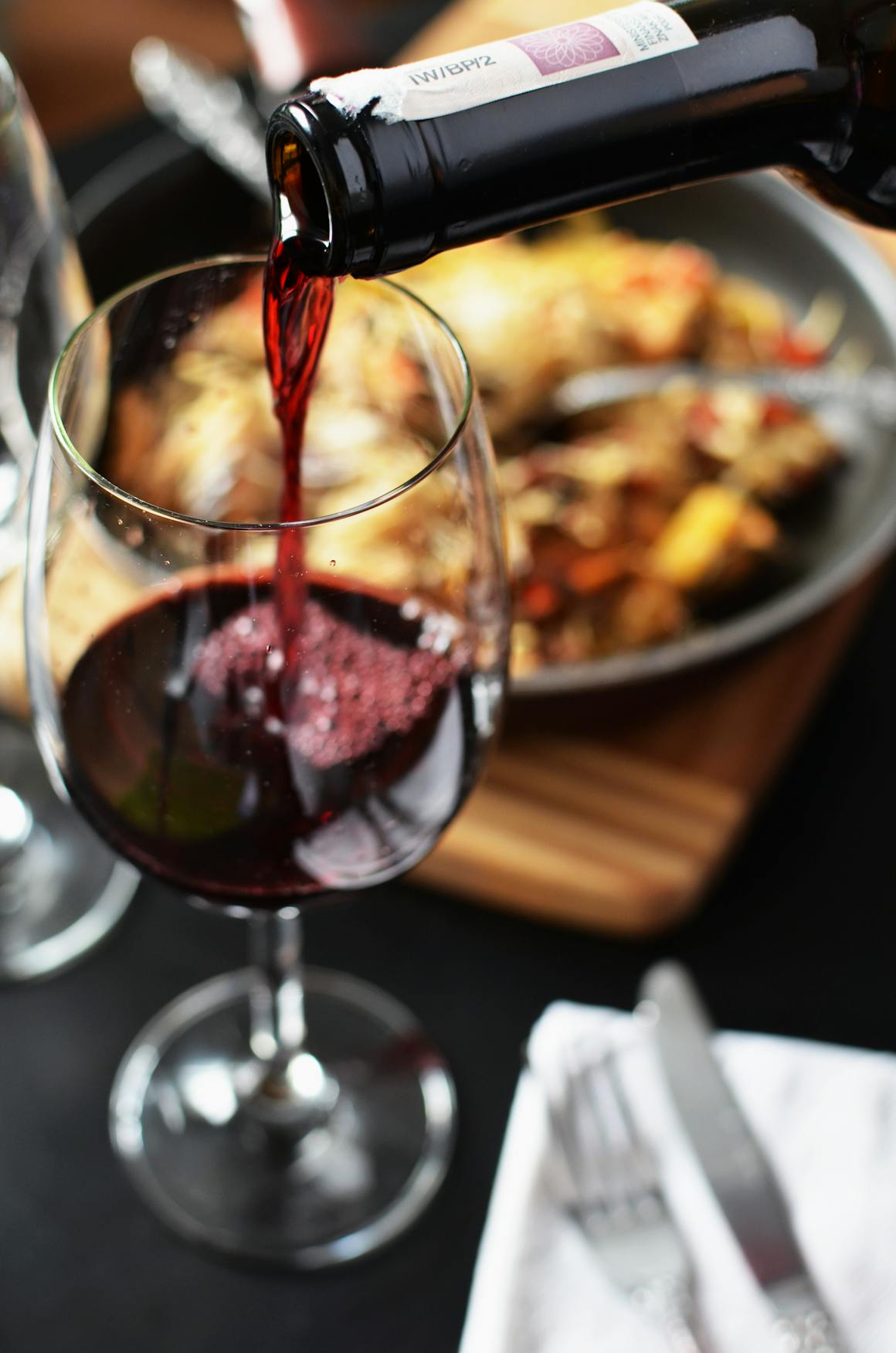 Close-up of red wine being poured into a glass at a romantic dinner setting with food in the background.