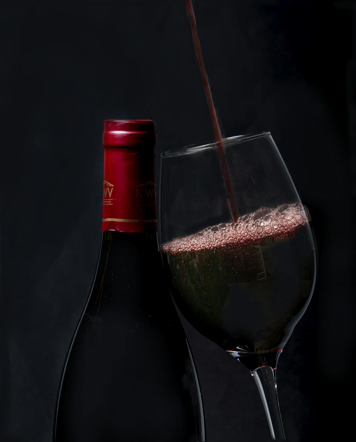 Elegant red wine pouring into a glass with a bottle in background, perfect for wine enthusiasts.