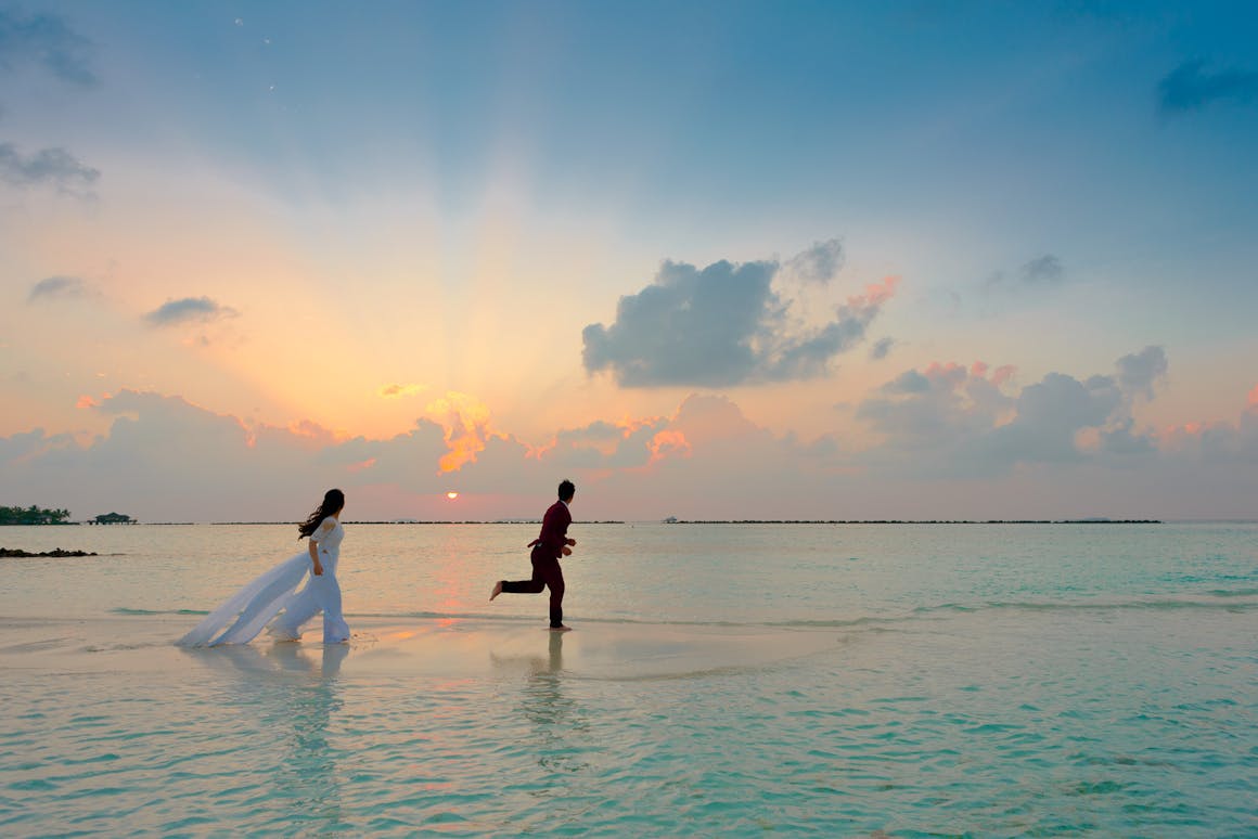 A couple enjoys a romantic moment running on a tropical beach during sunrise, capturing love and joy.