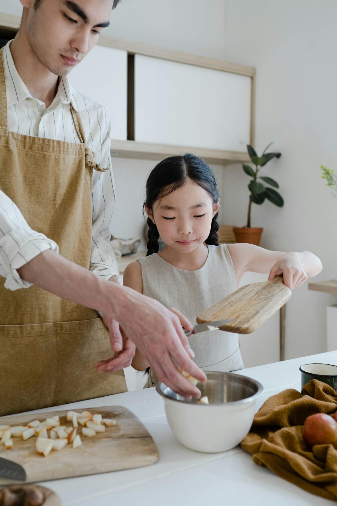Asian father and daughter baking together in a cozy kitchen setting.